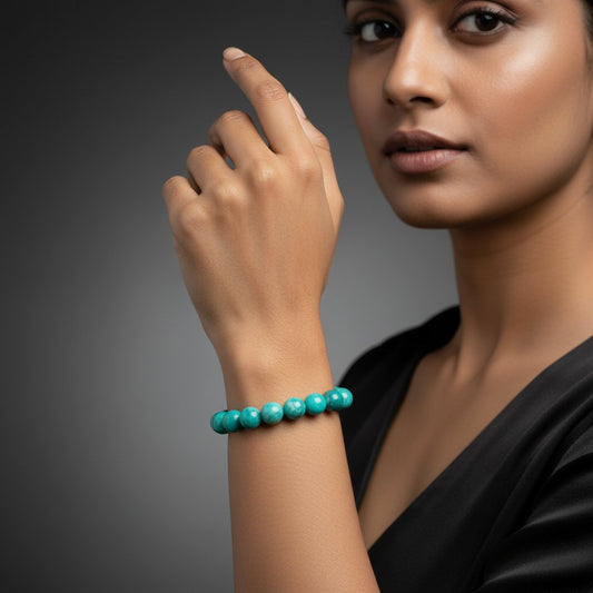 Turquoise beaded bracelet on wrist of person in black top against gray background