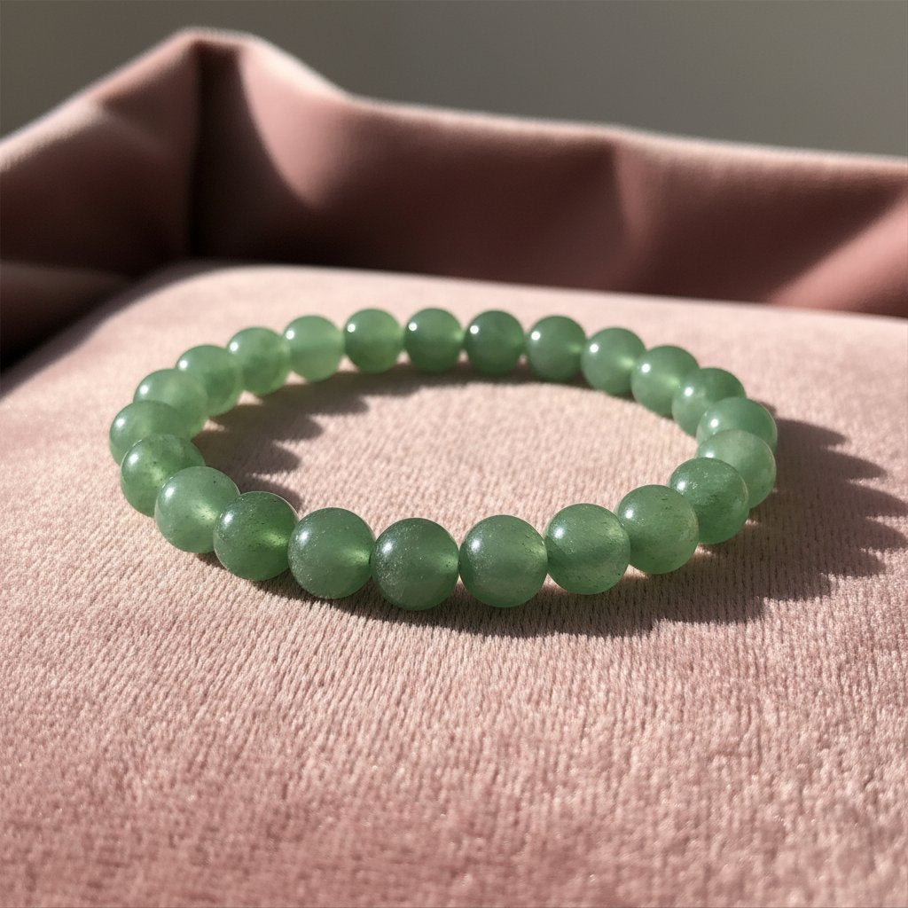 Green aventurine beaded bracelet with soft, uniform spherical stones resting on a blush pink textured fabric background.