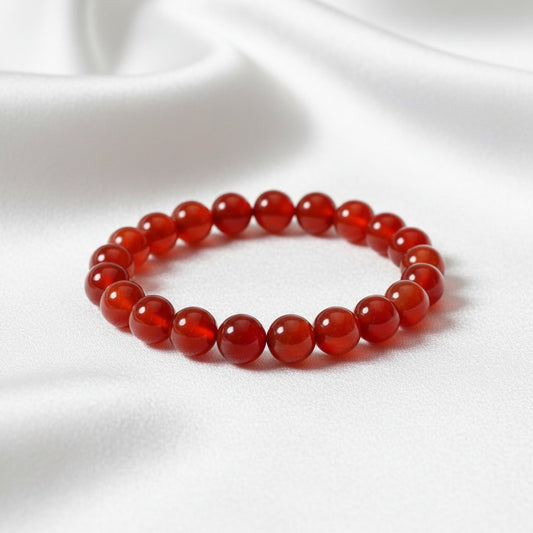 Elastic bracelet made of smooth, round, glossy red carnelian or agate gemstone beads against white fabric background