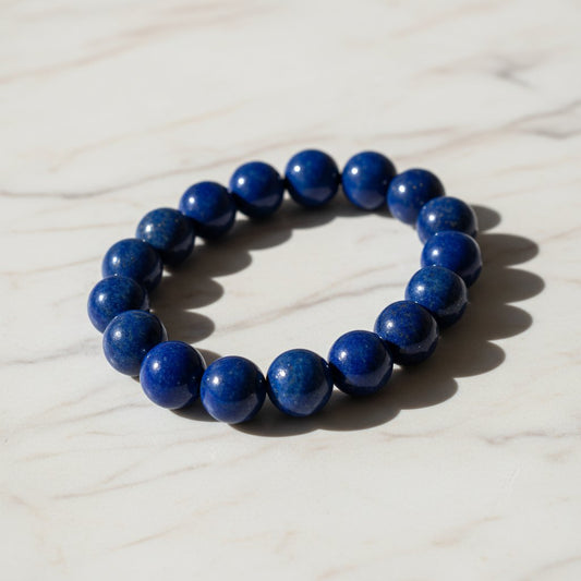 Deep blue lapis lazuli beaded bracelet arranged in a circular shape on a light marble background.