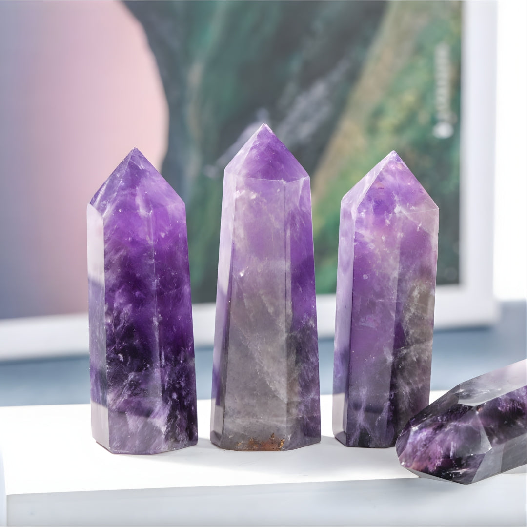Three polished amethyst crystal points with deep purple hues, standing upright on a white surface with a blurred green background.