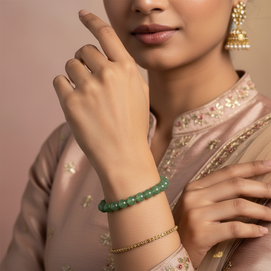 Woman in embroidered saree wearing green beaded bracelet and gold jhumka earring, hand positioned elegantly